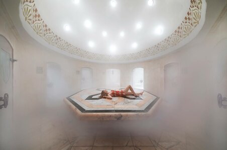 Eine Person liegt entspannt auf einer beheizten Steinliege im dampfigen Hamam.