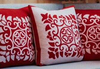 Three red and white patterned cushions are arranged on a bed in a hotel room.