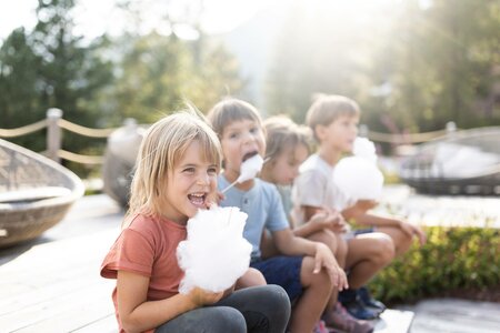 Mehrere Kinder sitzen draußen in der Sonne und essen Zuckerwatte während des Familienurlaubs im Hotel Hochschober.
