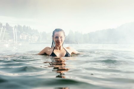 Eine Frau steht im Wasser des See-Bads vor der Uferkulisse am Hotel Hochschober.