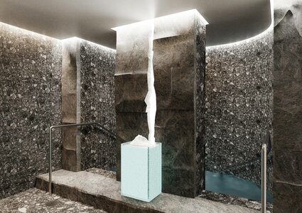 A serene spa interior featuring dark stone walls and a minimalist design. In the center, a tall, illuminated water feature flows from a square pedestal. Soft lighting enhances the tranquil atmosphere, while a small pool of water is visible in the background.