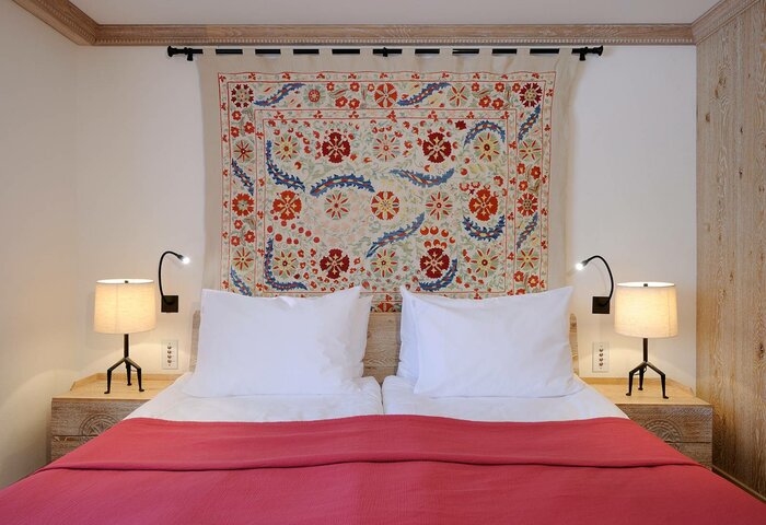 Comfort double room in the main building A double bed with white pillows, a red bedspread and a textile wall hanging in the comfort room of the main building.