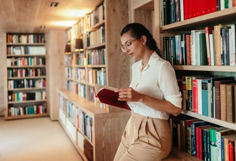 Eine Frau liest in einer ruhigen Hotelbibliothek zwischen hohen Bücherregalen.
