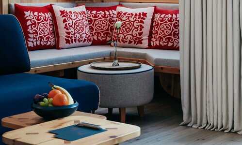 Ein Loungebereich mit blauem Sessel, Rundtisch und Sitzbank mit roten Kissen im Hotel Hochschober.