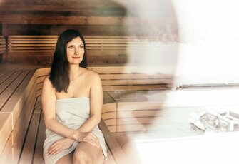 A woman sits in the wood-lined sauna and looks ahead calmly.