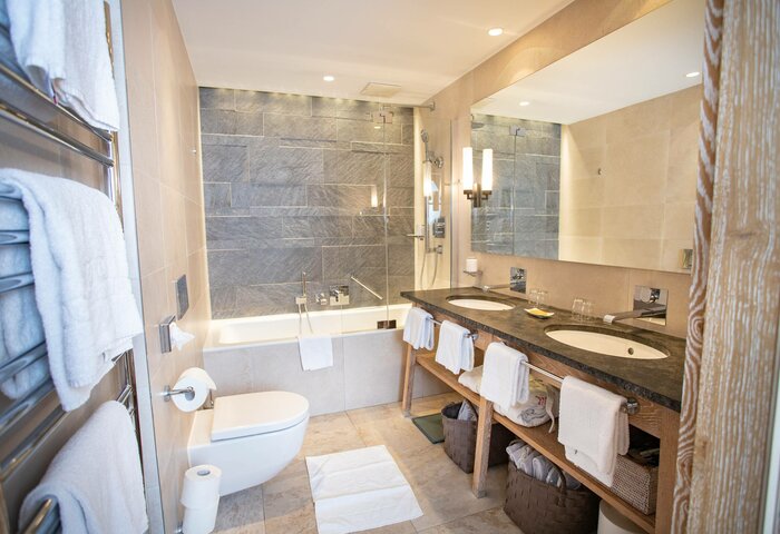 A bright bathroom with a bathtub, double sink vanity, towel rack and large wall mirrors.