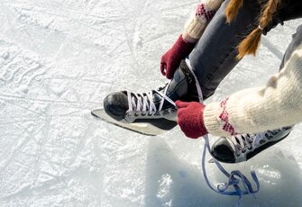 Eine Person zieht auf einer Eisfläche die Schlittschuhe fest.