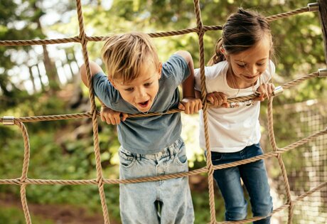 Zwei Kinder klettern auf einem Seilnetz und halten sich an den Seilen fest.