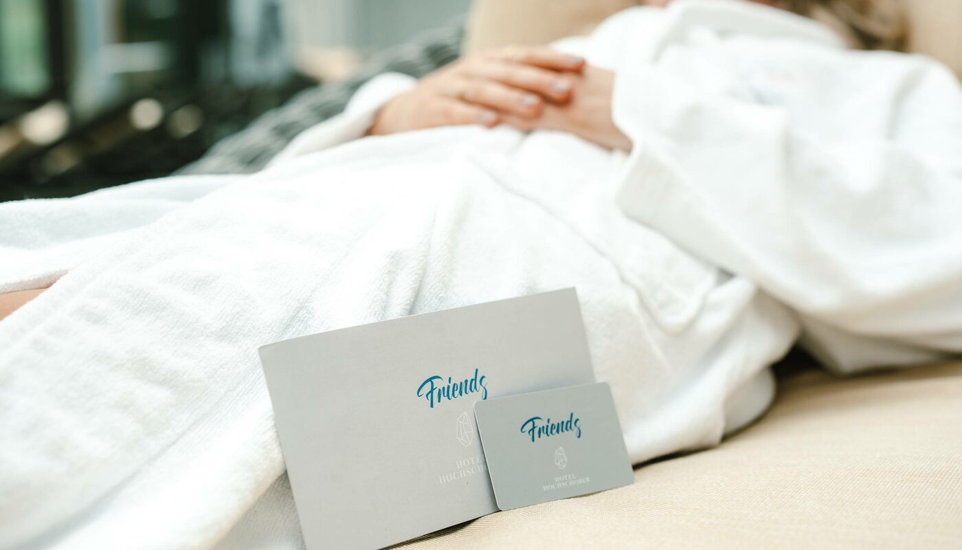 A person lies on a lounger in a white bathrobe, with two cards labeled “Friends” in the foreground.