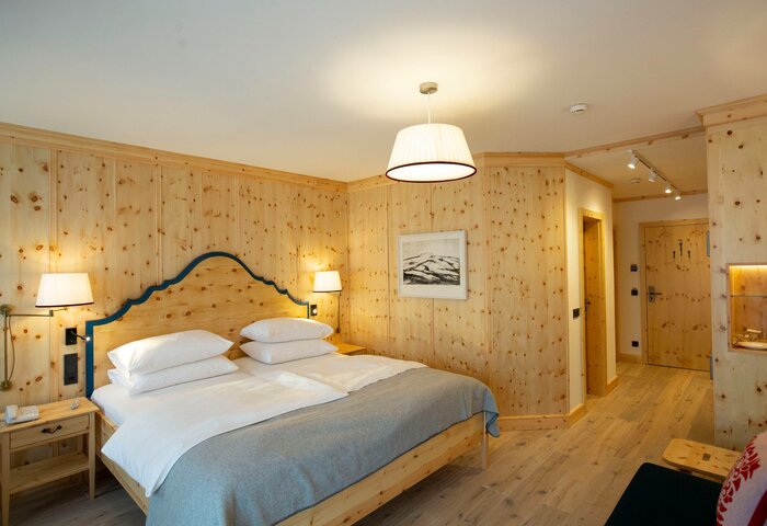 Ein helles Superior Zirbenzimmer mit Doppelbett, Holzvertäfelung, Nachttischen und Blick in den Flur.