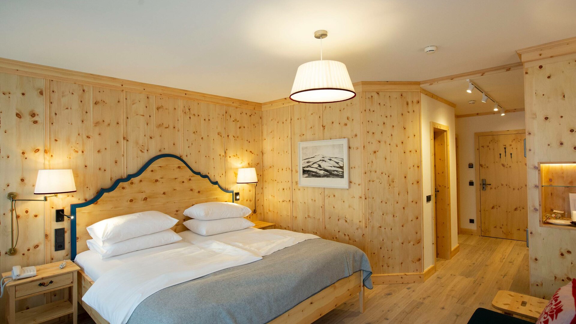 Ein helles Superior Zirbenzimmer mit Doppelbett, Holzvertäfelung, Nachttischen und Blick in den Flur.