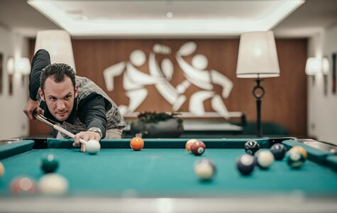 Ein Mann spielt Billard an einem grünen Tisch im stilvollen Billardzimmer des Hotel Hochschober.