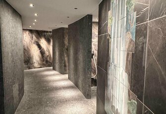 A modern sauna corridor with dark stone walls and lit wall murals at Hotel Hochschober.