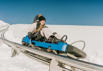 Eine Frau fährt mit dem Nocky Flitzer auf der verschneiten Strecke der Sommerrodelbahn.