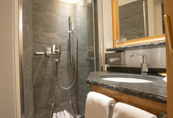 A modern bathroom with a shower, sink, towels and a folded laundry basket in the maisonette apartment.
