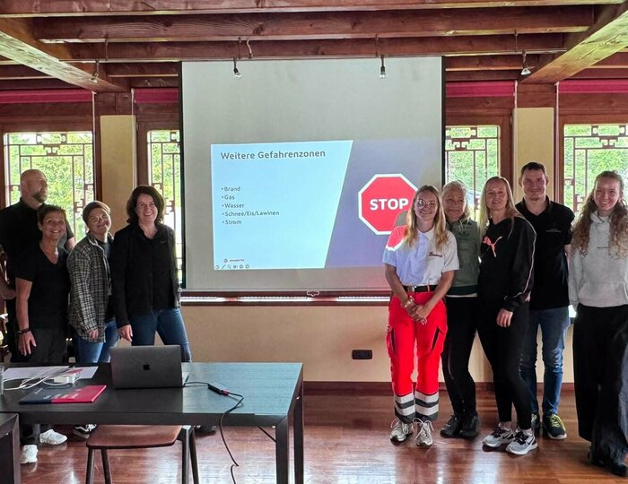 Praktikumsbetrieb im Hotel Hochschober Eine Gruppe von Personen steht vor einer Projektionswand in einem Holzraum mit roten Säulen; auf der Folie ist ein STOP-Schild zu sehen.
