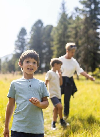 Eine Familie mit Kindern und Oma wandert im Herbst durch eine sonnige Wald- und Berglandschaft auf der Turracher Höhe.