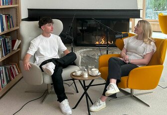 Two people sit by the fireplace in a library during a podcast recording.