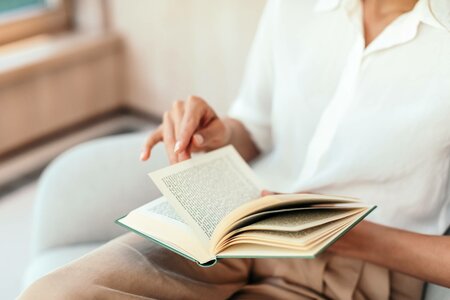 Eine Person blättert in einem offenen Buch in einer hellen Sitzgelegenheit der Hotelbibliothek.
