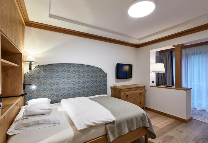 Single Room at Hotel Hochschober A neatly furnished single room at Hotel Hochschober with a bed, wooden furniture, patterned headboard and an opening to the next room.