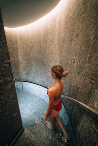 Eine Frau steht in einem warmen Becken im Hamam mit geschwungenen Steinwänden im Hotel Hochschober.
