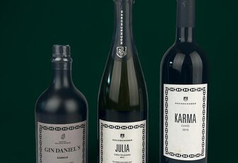 Three elegant Hotel Hochschober bottles stand against a dark green background.