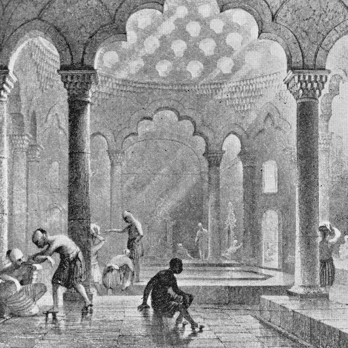An oriental hamam with columns, steam and several guests in a calm bathing hall.