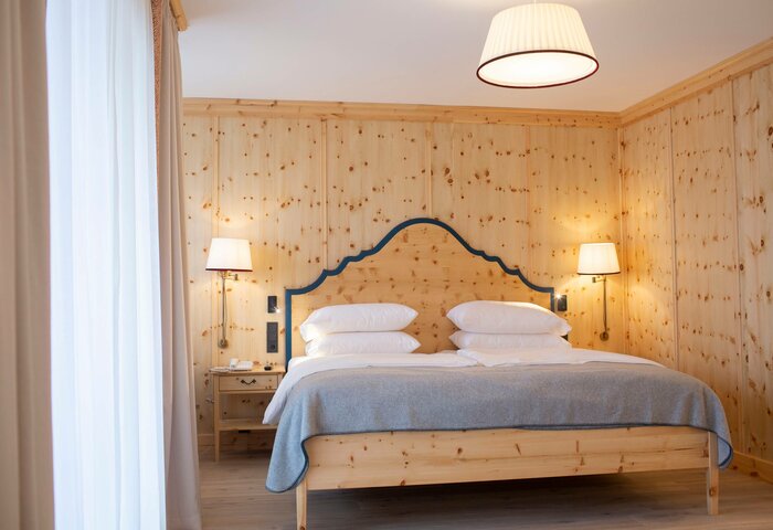 Deluxe stone pine room at Hotel Hochschober A double bed with a blue headboard stands in a wood-paneled deluxe stone pine room with bedside tables and lamps.