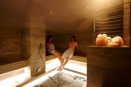 Ein Paar sitzt entspannt im warm beleuchteten Hamam mit Natursteinwänden und Handtüchern.