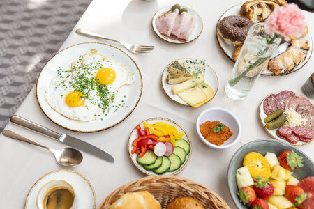 Ein reich gedeckter Frühstückstisch mit Spiegeleiern, Brot, Aufschnitt, Käse, Obst, Gemüse und Kaffee.
