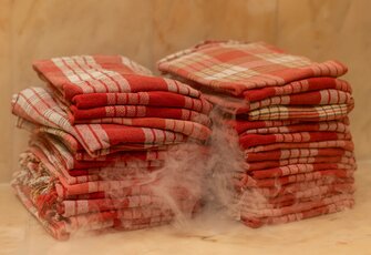 Several stacked red checkered towels lie on a warm surface, with steam rising between them.