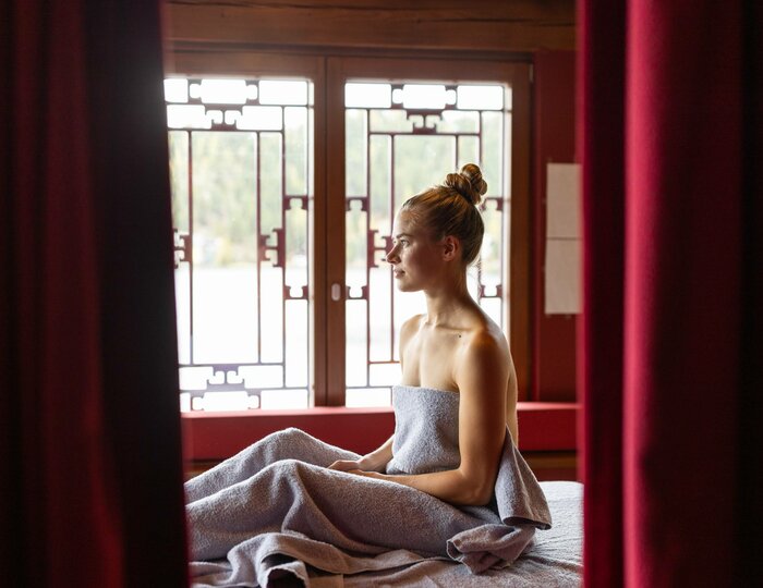 Eine Frau sitzt in ein Handtuch gewickelt auf einer Massageliege im Kristall Spa.