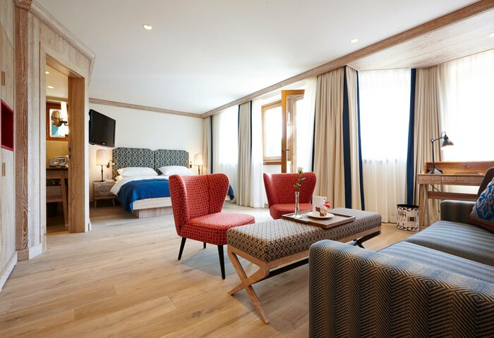 Das Deluxe Bergkristall Zimmer im Hotel Hochschober zeigt Schlafbereich, Sitzgruppe und große Fenster mit Vorhängen.