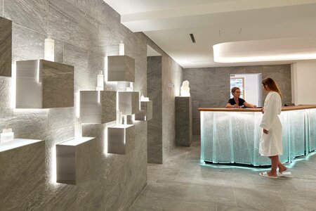 Im Kristall Spa stehen beleuchtete Steinquader und ein Empfangstresen, an dem eine Frau im Bademantel steht.
