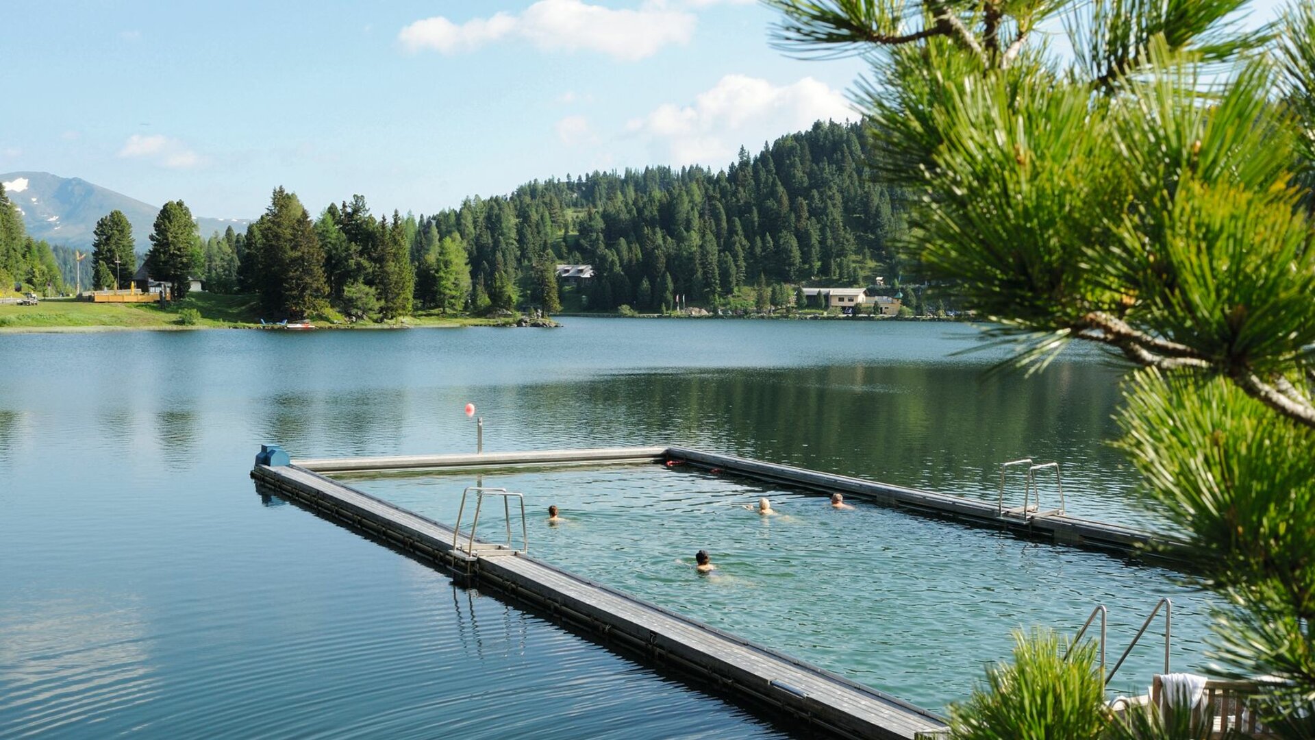 A heated lake pool sits in Lake Turracher, with a floating platform, calm water and forested hills behind it.