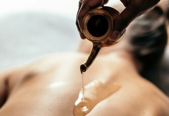 Eine Hand gießt Öl aus einem kleinen Gefäß auf den Rücken einer Person während einer Spa-Massage.