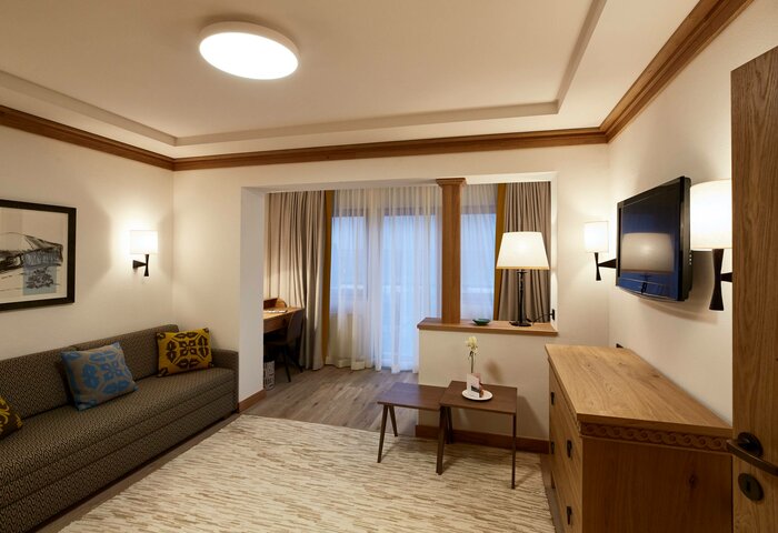 The family apartment studio shows a living area with sofa, table and TV, plus a sleeping area by the window.