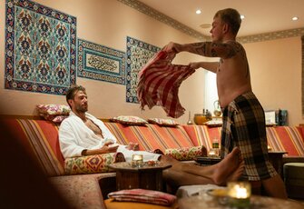 A guest is being treated in an oriental-style hamam while another guest sits nearby.