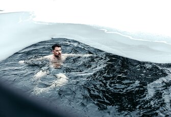 Ein Mann schwimmt im beheizten See-Bad des Hotel Hochschober, umgeben von dunklem Wasser und hellem Eisrand.