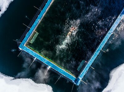 Eine Person schwimmt in einem quadratischen, beheizten See-Bad auf dunklem Wasser.
