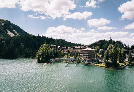Hotel Hochschober stands on the shore of Lake Turracher See, surrounded by forest and mountains.