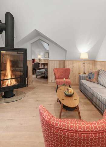 A cozy suite living room with a fireplace, sofa, armchair and light wood flooring.