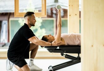Ein Trainer unterstützt eine Frau bei einer Übung auf der Trainingsbank im Fitnessraum.