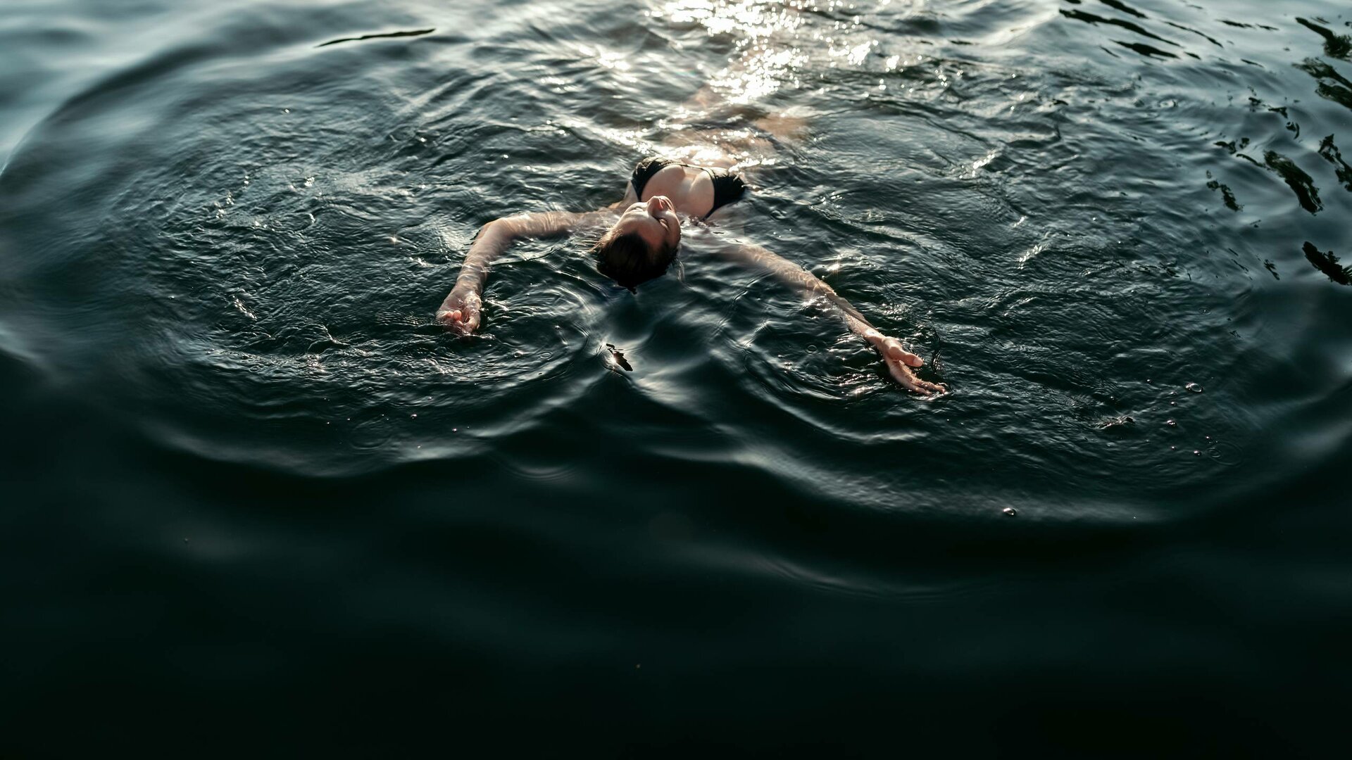 Eine Person schwimmt auf dem Rücken im dunklen Wasser des Sees.