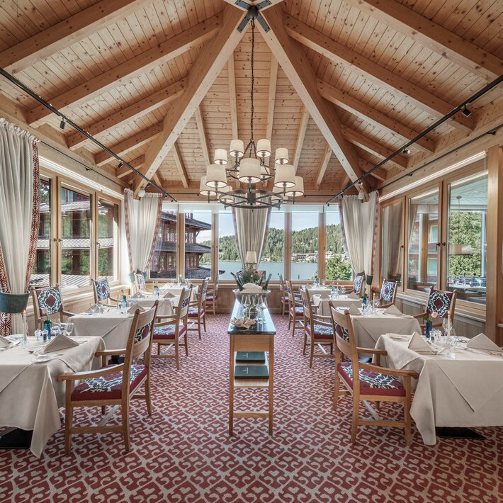 Ein helles Restaurant mit gedeckten Tischen, Holzdach und Blick auf den See.