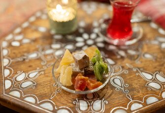 A glass of red tea and a small bowl of dried fruit sit on an ornately patterned wooden table.