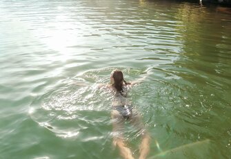 Eine Frau schwimmt im beheizten See-Bad auf dem Turracher See, umgeben von ruhigem Wasser.