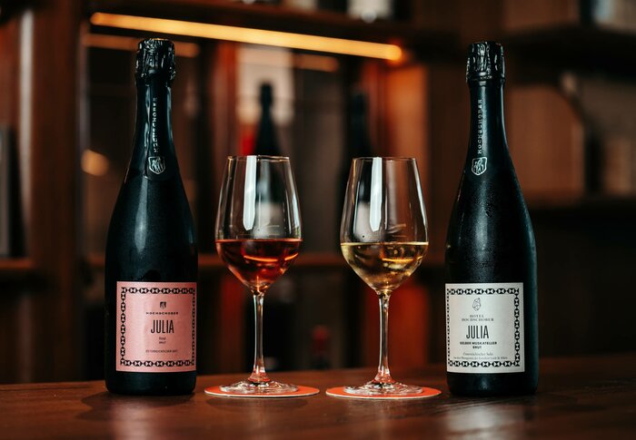 Two sparkling wine bottles and two filled wine glasses are arranged on a wooden table in the hotel shop.