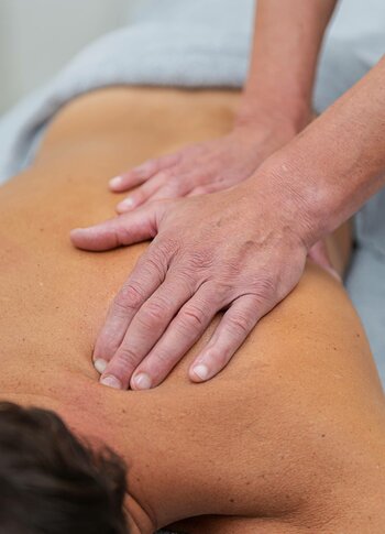 Zwei Hände massieren den Rücken einer liegenden Person bei der Kräuterölmassage im Kristall Spa.