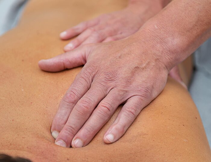 Two hands massage the back of a lying person during a herbal oil massage at Kristall Spa.